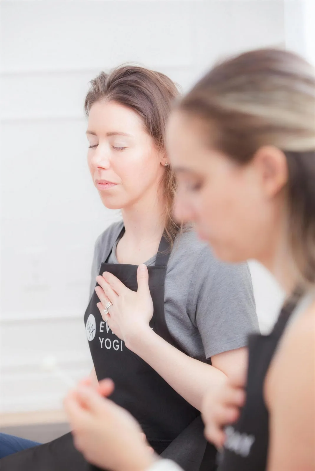 Two people in Everyday Yogi aprons resting hand-on-heart in quiet practice